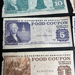 May include: Three vintage US Department of Agriculture food coupons. The top coupon is blue and white and has a value of 10 dollars. The middle coupon is blue and white and has a value of 5 dollars. The bottom coupon is brown and white and has a value of 1 dollar.