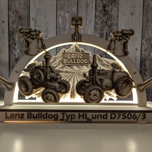 Könnte beinhalten: Beleuchtete Holzdekoration mit zwei Traktorillustrationen. Das Design enthält den Text "Lanz Bulldog" und "Lanz Bulldog Typ HL und D7506/3". Das Stück zeigt eine Berglandschaft und dekorative Elemente.