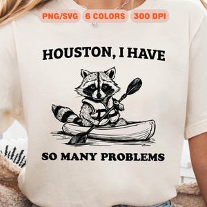Può includere: Illustrazione in bianco e nero di un procione che indossa un giubbotto di salvataggio e rema in canoa. Il testo "Houston, ho così tanti problemi" è scritto sopra il procione.