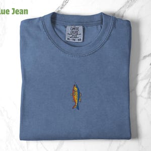 May include: A blue jean t-shirt with a colourful fish graphic and the text "COMFORT COLORS XL - TG - EG" on the tag.