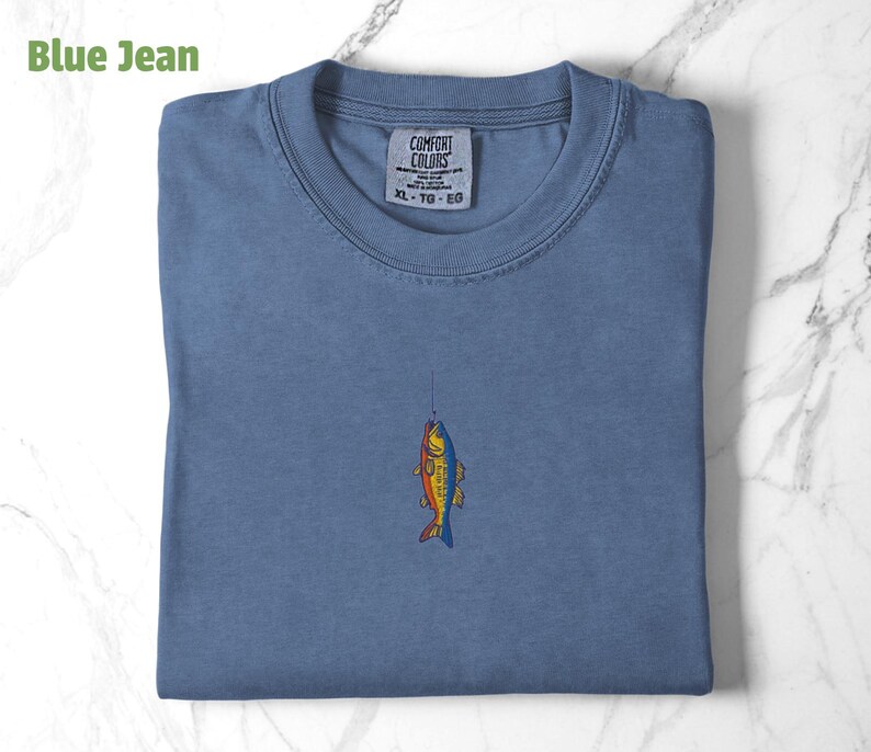 May include: A blue jean t-shirt with a colourful fish graphic and the text "COMFORT COLORS XL - TG - EG" on the tag.