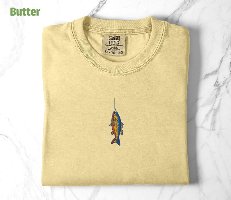 May include: A yellow t-shirt with a small embroidered image of a fish on a fishing line. The shirt has a tag that says "Comfort Colors" and "XL - TG - EG".