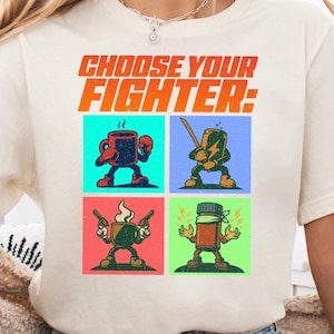 May include: A white t-shirt with the text "Choose Your Fighter:" printed on the front. The text is in a bold, orange font. Below the text are four colorful squares, each containing a cartoon character. The characters are a coffee cup, a can of soda, a coffee mug, and a pill bottle. Each character is depicted in a fighting pose.