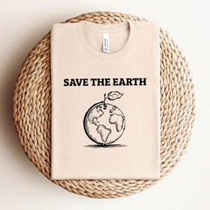 May include: A beige t-shirt with the text "Save the Earth" and a black and white illustration of the Earth with a leaf growing from it.