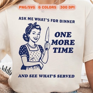 May include: A white t-shirt with a blue graphic of a woman holding a knife. The text on the shirt reads "Ask me what's for dinner one more time and see what's served."