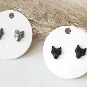 Könnte beinhalten: Zwei Paar Wolfskopf-Ohrstecker. Ein Paar ist silberfarben und das andere schwarz.