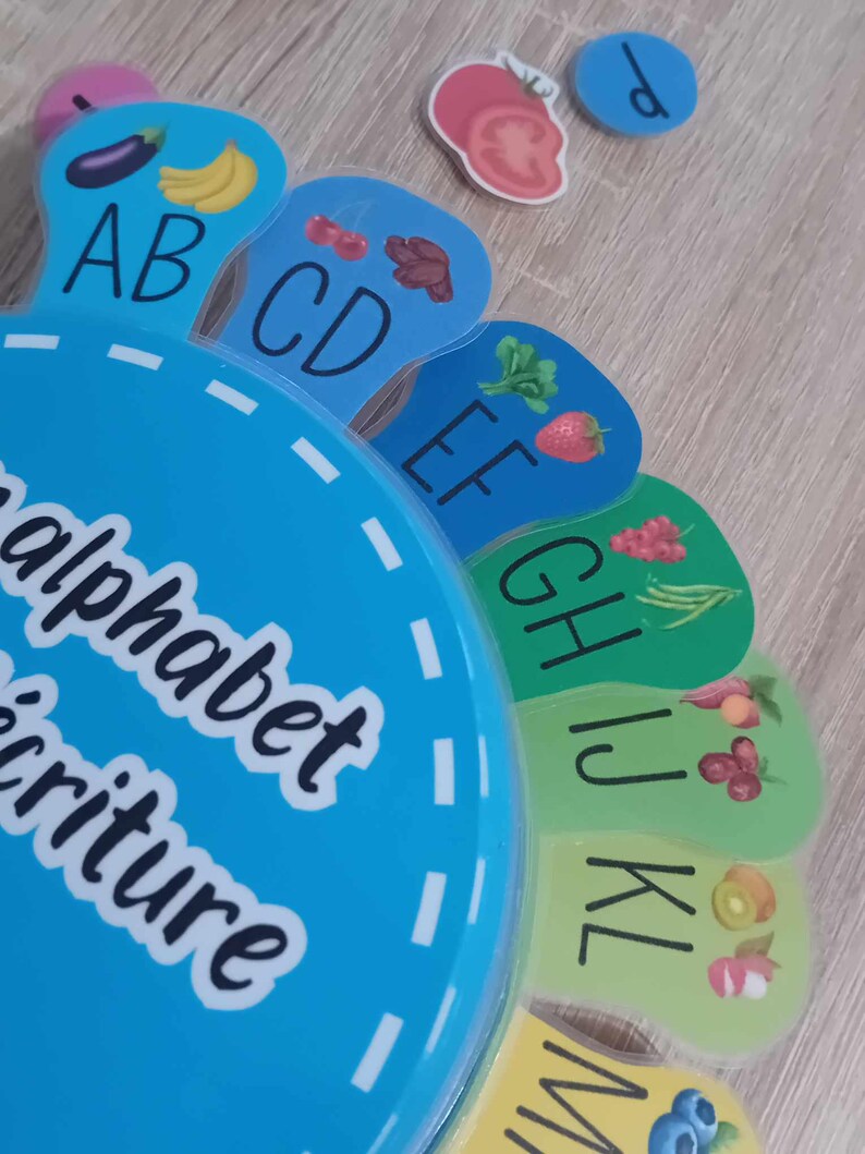 May include: A colorful alphabet learning toy with a blue base and colorful segments featuring letters and pictures of fruits and vegetables. The text on the base reads "alphabet scripture".