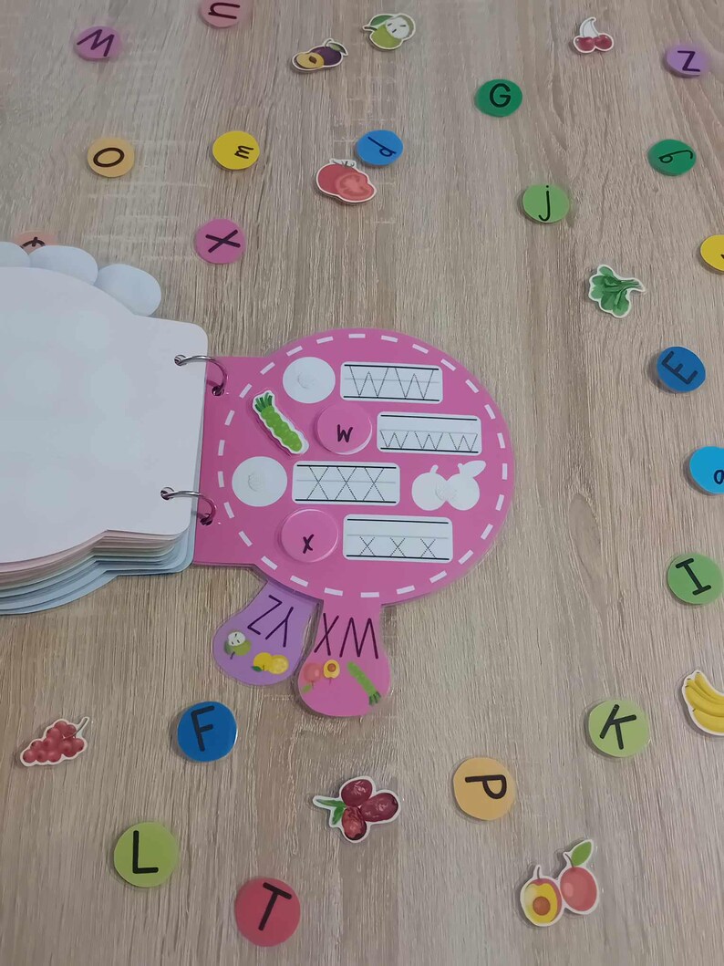 May include: Pink alphabet learning toy with a book and letter tiles. The book has pages with letters and lines for tracing. The tiles are colorful and have letters on them.
