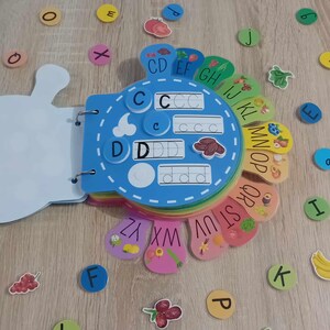 May include: A colorful alphabet learning toy with a blue center and rainbow-colored outer rings. Each ring has a letter and a picture of a fruit or vegetable. The letters are written in uppercase and lowercase. The toy is designed for children to learn the alphabet.