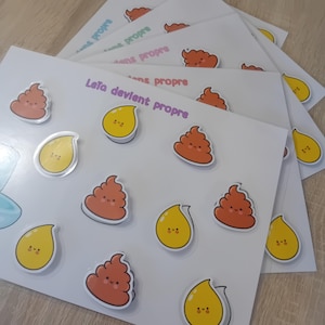 Peut inclure: Plusieurs cartes blanches avec des autocollants de dessins animés représentant des larmes jaunes souriantes et des emojis de caca marron souriants. Le texte "Leta devient propre" est imprimé en violet sur les cartes. Les cartes sont empilées.