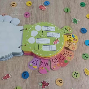 May include: A colorful alphabet learning toy with a green, yellow, and orange base. The toy has a circular shape with different colored sections that feature letters of the alphabet. Each section has a different fruit or vegetable design. The toy is designed for children to learn the alphabet.