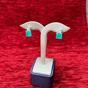 Peut inclure: Une paire de boucles d'oreilles en &eacute;meraude verte et en pierres pr&eacute;cieuses blanches sur un pr&eacute;sentoir. Les boucles d'oreilles sont serties d'argent et ont une forme carr&eacute;e.