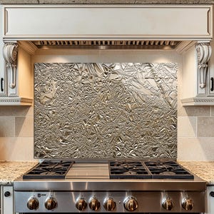 Puede incluir: Una cocina de gas de acero inoxidable con un protector contra salpicaduras de metal texturizado. La cocina cuenta con gabinetes blancos con molduras decorativas, una encimera de granito y un bloque de cuchillos de madera. La cocina tiene seis quemadores.