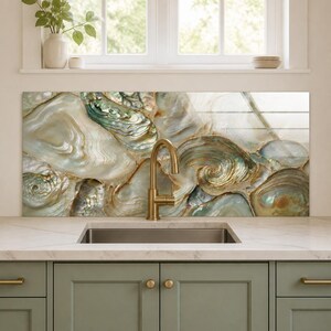 Op de afbeelding: Een keukenachterwand met een hoogglansprint van iriserende abalone-schelpen met wervelende patronen in crème, goud en groenblauw. Een messingkleurige metalen kraan is voor het paneel gemonteerd boven een rechthoekige roestvrijstalen spoelbak.