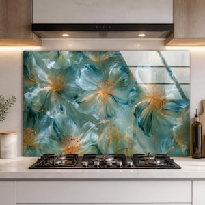May include: A rectangular glass kitchen backsplash panel featuring a large-scale floral print with translucent teal and blue petals and golden-yellow centers. The artwork displays soft, painterly brushstrokes and a glossy finish, positioned behind a black gas stovetop.