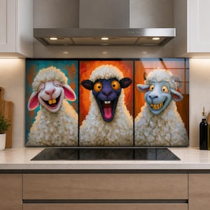 Op de afbeelding: Een driedelige keukenachterwand met cartoon-schapen met expressieve gezichten. Het linkerpaneel toont een lachend wit schaap, het middenpaneel een verrast schaap met een zwart gezicht en het rechterpaneel een grijnzend schaap met een blauw gezicht.