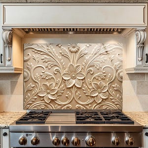 May include: A beige kitchen backsplash featuring a raised floral design. The image shows a stainless steel gas hob, granite worktops, and white cabinets. The floral pattern is in white relief, adding a decorative element.