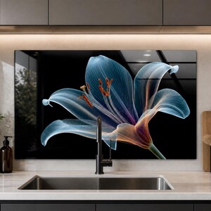 May include: A rectangular glass kitchen backsplash panel featuring a large, translucent blue lily flower with visible veins and orange stamens set against a solid black background, positioned behind a stainless steel sink and a black faucet.