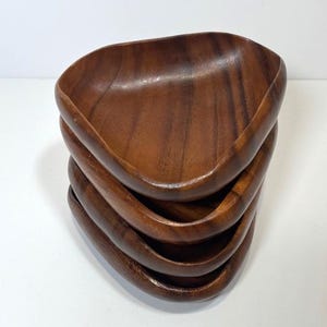 May include: A stack of four wooden bowls. Each bowl has a triangular shape with rounded edges and a rich, brown colour. The wood grain is visible, adding to the natural aesthetic. The bowls are stacked on top of each other.
