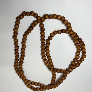May include: A necklace composed of many small, round, wooden beads. The beads are a warm brown hue and strung together to create a long strand. The necklace is shown against a white backdrop.