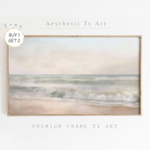 May include: A framed painting of a seascape with soft, pastel colors. The painting depicts a beach with waves crashing on the shore. The sky is a light blue with hints of pink and purple. The painting is framed in a simple wooden frame.