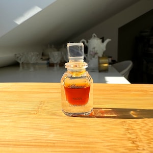 Könnte beinhalten: Eine kleine, durchsichtige Glasflasche mit Chopard Happy Diamonds Parfum. Die Flasche ist mit einer goldbraunen Flüssigkeit gefüllt und hat einen durchsichtigen Glasverschluss.