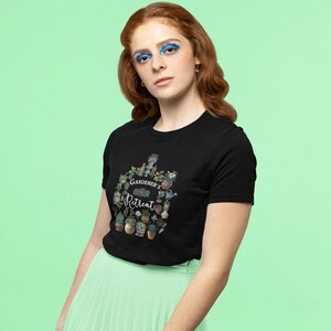May include: A black t-shirt with a graphic design of a circle of potted plants and gardening tools. The text "GARDENER'S RETREAT" is in the center of the design.