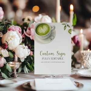 Op de afbeelding: Een wit aangepast bord met de tekst "Custom Sign FULLY EDITABLE" en een aquarel illustratie van een matcha latte met een hartvormig ontwerp. Het bord wordt weergegeven op een heldere standaard, omringd door bloemen en kaarsen.