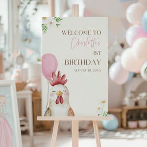 Op de afbeelding: Een welkomstbord voor een eerste verjaardag. Het bord toont de tekst "Welcome to Charlotte's 1st Birthday" met een aquarel illustratie van een kip met een roze ballon. Madeliefjes en groen decoreren de boven- en onderkant.
