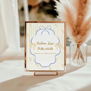 Op de afbeelding: Een ingelijst aangepast bord met een goudkleurig frame. Het bord heeft een lichtgele en witte gestreepte achtergrond met citroenillustraties. Het bord heeft een blauw-witte decoratieve rand met de tekst "Custom Sign, Fully editable".
