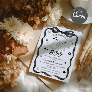 Könnte beinhalten: Eine schwarz-weiße Einladung mit dem Text "She found her BOO" und zwei Geisterillustrationen. Die Einladung enthält Eventdetails und ist mit Herzen, Sternen und Blumen verziert. Die Einladung ist von getrockneten Blumen und Blättern umgeben.