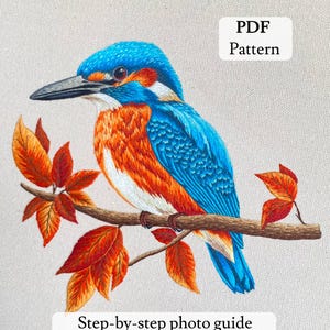 以下が含まれることがあります： 秋の葉が付いた枝に止まっているカワセミの刺繍アート。鳥は青、オレンジ、白の羽毛を持っています。「PDF Pattern」と「Step-by-step photo guide」の文字が見えます。