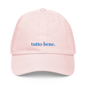 May include: A pink baseball cap with the phrase "tutto bene." embroidered in blue.
