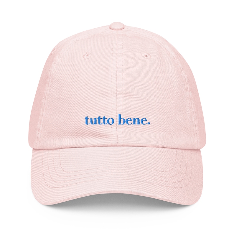 May include: A pink baseball cap with the phrase "tutto bene." embroidered in blue.