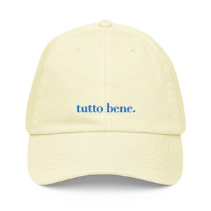 May include: A light yellow baseball cap with the phrase "tutto bene." embroidered in blue.