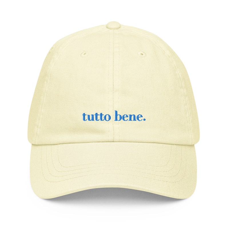 May include: A light yellow baseball cap with the phrase "tutto bene." embroidered in blue.
