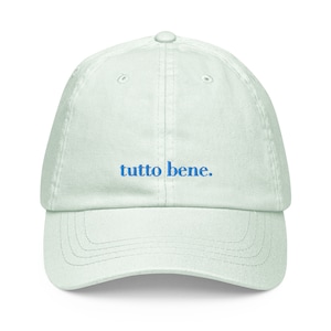 May include: A light green baseball cap with the phrase "tutto bene." embroidered in blue.