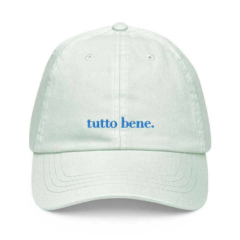 May include: A light green baseball cap with the phrase "tutto bene." embroidered in blue.