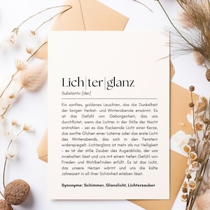 Può includere: Una carta bianca con il testo tedesco "Lichterglanz" e una definizione, appoggiata su una busta beige. Fiori secchi e baccelli di semi circondano la carta, creando un'estetica neutra e naturale.