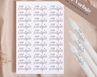 May include: A sheet of stickers with the text "KLEINER Weihnachtsgrüß" in a handwritten style, along with small star accents. The stickers are arranged in rows and columns. Several white candles with the same text are also visible.