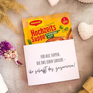 DIY-Verpackung für Tütensuppe mit Aufdruck zur Hochzeit, witzige Geschenkidee mit Text „Ab jetzt müsst ihr die Suppe gemeinsam auslöffeln“ bzw. „Für alle Suppen, die das Leben serviert“, dekoriert mit Trockenblumen, Herzdeko und Kerze – ideal als Printable zur Hochzeit.