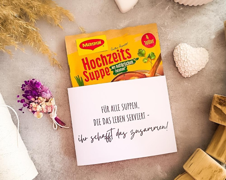 DIY-Verpackung für Tütensuppe mit Aufdruck zur Hochzeit, witzige Geschenkidee mit Text „Ab jetzt müsst ihr die Suppe gemeinsam auslöffeln“ bzw. „Für alle Suppen, die das Leben serviert“, dekoriert mit Trockenblumen, Herzdeko und Kerze – ideal als Printable zur Hochzeit.