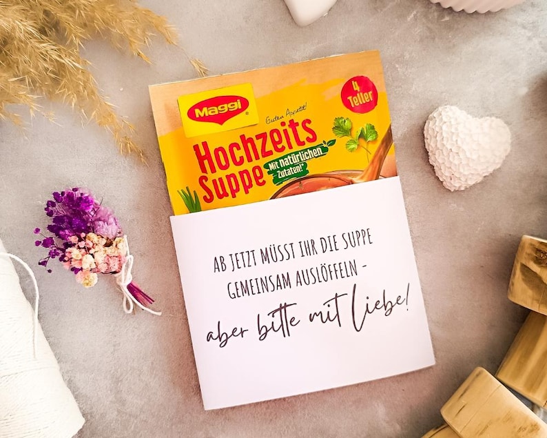 DIY-Verpackung für Tütensuppe mit Aufdruck zur Hochzeit, witzige Geschenkidee mit Text „Ab jetzt müsst ihr die Suppe gemeinsam auslöffeln“ bzw. „Für alle Suppen, die das Leben serviert“, dekoriert mit Trockenblumen, Herzdeko und Kerze – ideal als Printable zur Hochzeit.