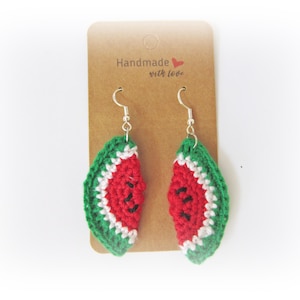 May include: Handmade crochet watermelon earrings with silver-colored hooks. The earrings feature a red center with black seeds, a white rind, and a green outer edge. The earrings are displayed on a brown card with the text "Handmade with love."