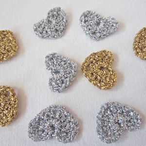 Könnte beinhalten: Eine Sammlung von zehn gehäkelten Herzen in Silber und Gold. Die Herzen sind alle gleich groß und gleich geformt und in einem zufälligen Muster angeordnet.