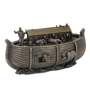 Könnte beinhalten: Eine bronzene Figur von Noahs Arche mit einer detaillierten Darstellung von Noah und verschiedenen Tieren an Bord. Die Arche ruht auf einem wellenförmigen Sockel.