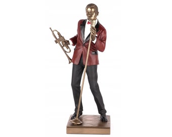 May include: A bronze sculpture of a man in a red suit holding a trumpet and a microphone. He is standing on a stage with a patterned floor.