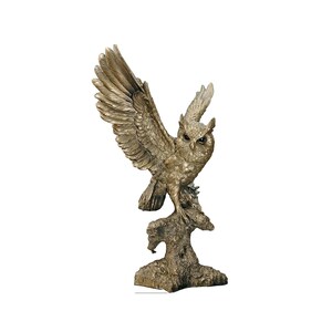 Op de afbeelding: Een gouden uilbeeldje met gespreide vleugels, gepercht op een boomstronk. De uil heeft gedetailleerde veren en realistische ogen.