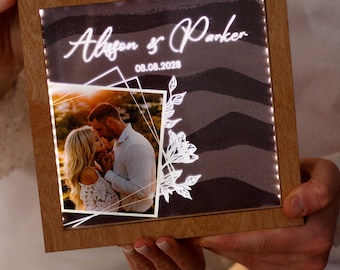 May include: A wooden framed photo with the names "Alison & Parker" and the date "08.08.2028" illuminated on the front. The photo features a couple kissing, with a white floral design and geometric shapes.