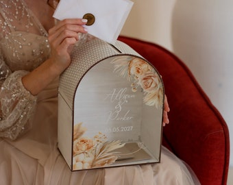 May include: A wooden wedding card box with an arched top and floral design. The box features the names "Allison & Parker" and the date "05.05.2027". The box is decorated with beige and peach-colored flowers and foliage.
